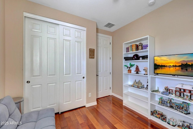 living area with built in features, baseboards, visible vents, and wood finished floors