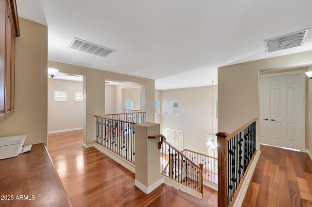 corridor with wood-type flooring, an upstairs landing, and visible vents