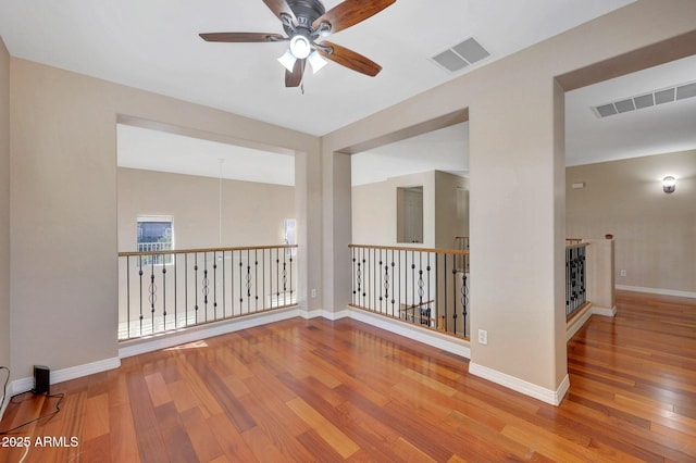 empty room featuring baseboards, visible vents, ceiling fan, and wood finished floors