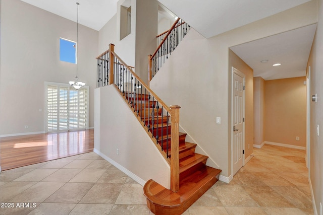 stairway featuring baseboards, tile patterned flooring, a towering ceiling, and a notable chandelier