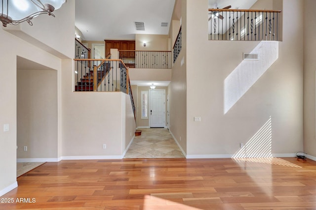 foyer entrance featuring a towering ceiling, wood finished floors, and visible vents