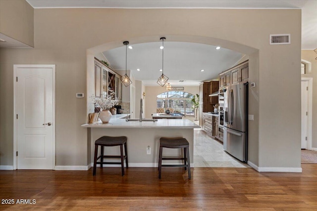 kitchen featuring visible vents, stainless steel fridge with ice dispenser, a breakfast bar area, a peninsula, and light wood-style floors