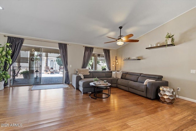 living area with vaulted ceiling, light wood-style flooring, a ceiling fan, and baseboards