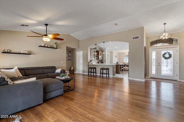 living room featuring visible vents, ceiling fan with notable chandelier, wood finished floors, arched walkways, and lofted ceiling