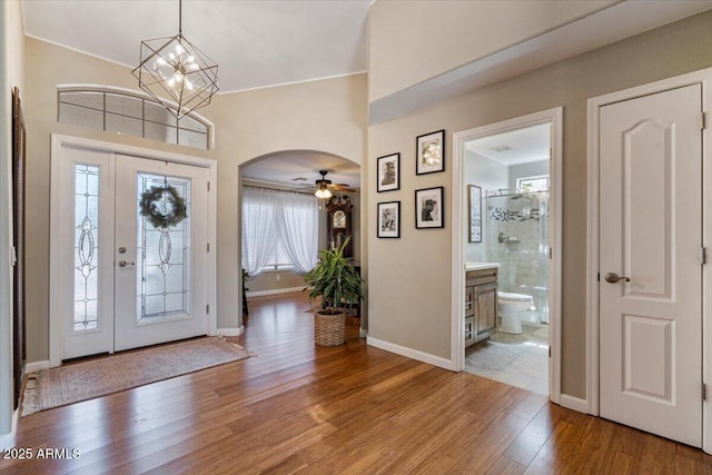 entryway with baseboards, arched walkways, an inviting chandelier, and wood-type flooring