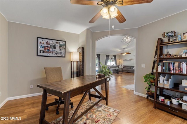 office featuring a ceiling fan, baseboards, arched walkways, and light wood finished floors