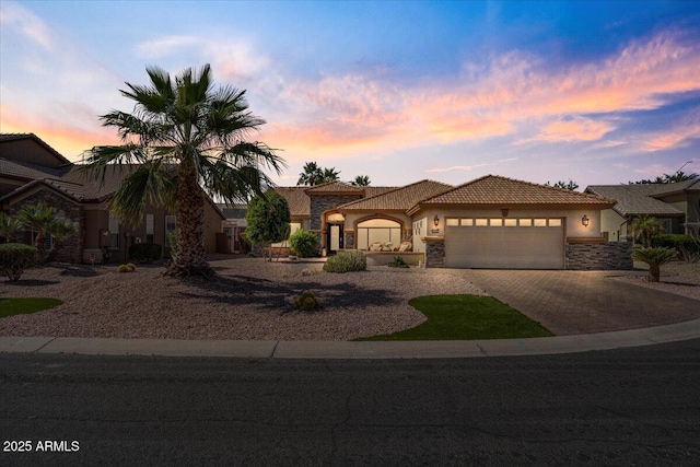 mediterranean / spanish-style home with driveway, an attached garage, stucco siding, stone siding, and a tile roof