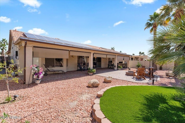 rear view of property with a fire pit, roof mounted solar panels, stucco siding, a fenced backyard, and a patio