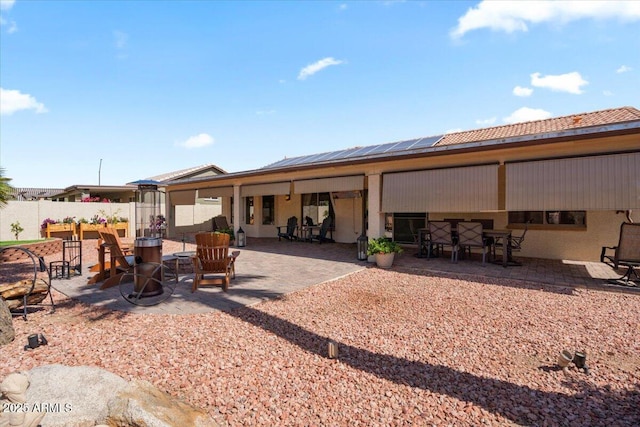 rear view of property featuring fence, an outdoor fire pit, solar panels, outdoor dining area, and a patio area