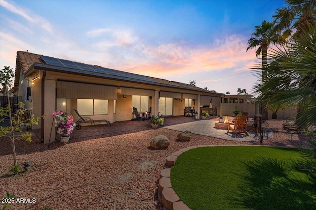 back of property at dusk with solar panels, stucco siding, a fire pit, a patio area, and a lawn