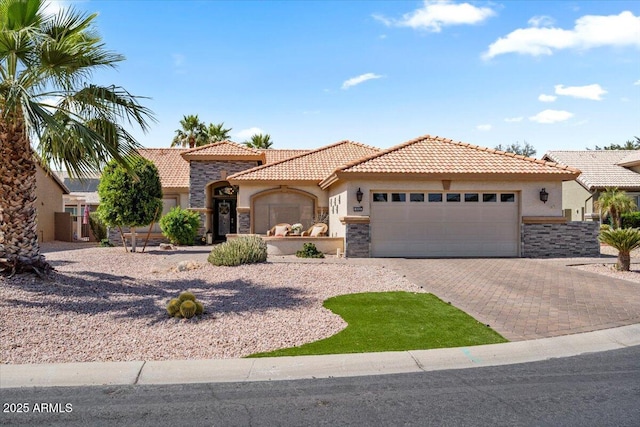 mediterranean / spanish house featuring stucco siding, stone siding, and an attached garage