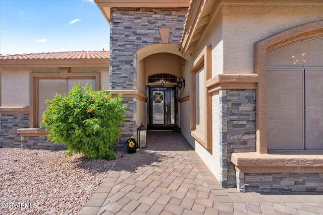 property entrance featuring stone siding, stucco siding, and a tile roof