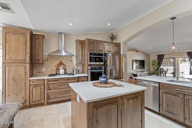 kitchen with visible vents, wall chimney range hood, vaulted ceiling, arched walkways, and stainless steel appliances