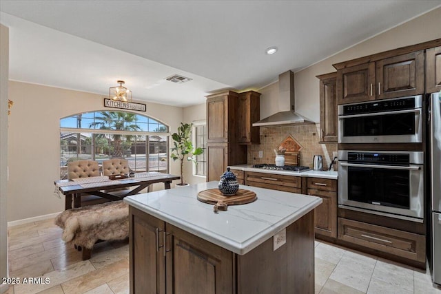 kitchen featuring visible vents, tasteful backsplash, a center island, appliances with stainless steel finishes, and wall chimney range hood