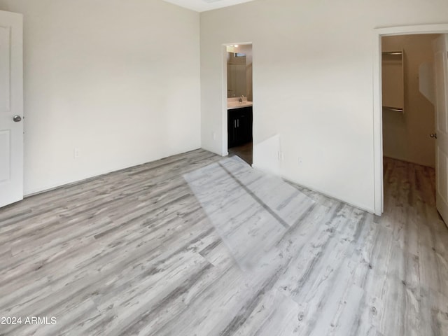 unfurnished bedroom featuring connected bathroom, light hardwood / wood-style floors, and sink