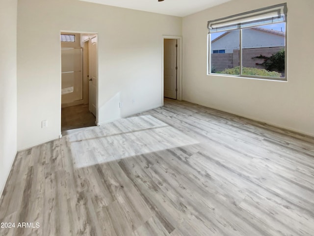 unfurnished bedroom with a walk in closet, a closet, ensuite bath, and light wood-type flooring