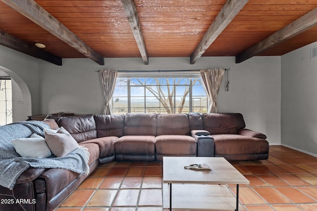 unfurnished living room with baseboards, beam ceiling, arched walkways, wood ceiling, and tile patterned floors