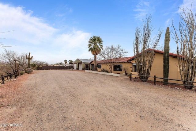 view of front of home with stucco siding, fence, and dirt driveway