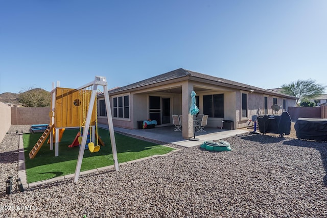 rear view of property featuring a playground and a patio area