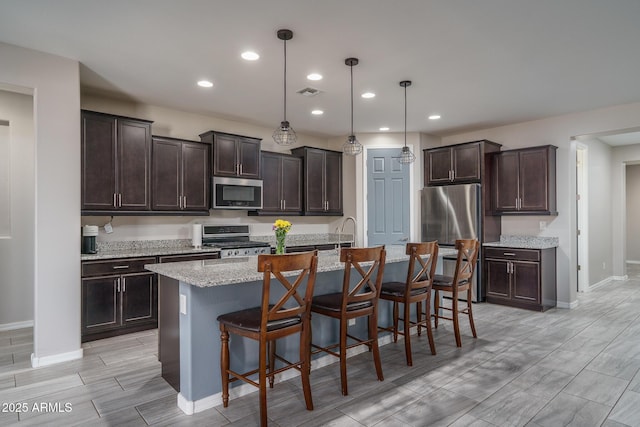 kitchen featuring a kitchen bar, stainless steel appliances, decorative light fixtures, a kitchen island with sink, and dark brown cabinets