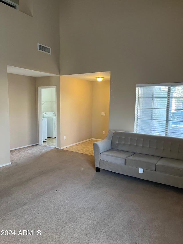 unfurnished living room featuring light colored carpet, a towering ceiling, and washer / clothes dryer