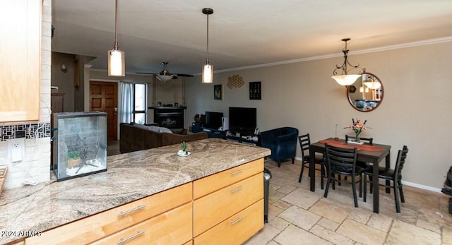 kitchen with pendant lighting, crown molding, ceiling fan, light stone countertops, and a fireplace