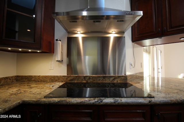 kitchen featuring dark brown cabinetry, light stone countertops, wall chimney exhaust hood, and cooktop