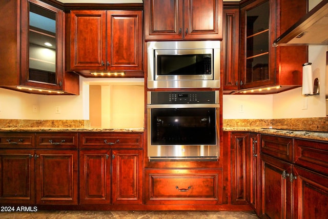 kitchen featuring light stone counters, appliances with stainless steel finishes, and wall chimney range hood