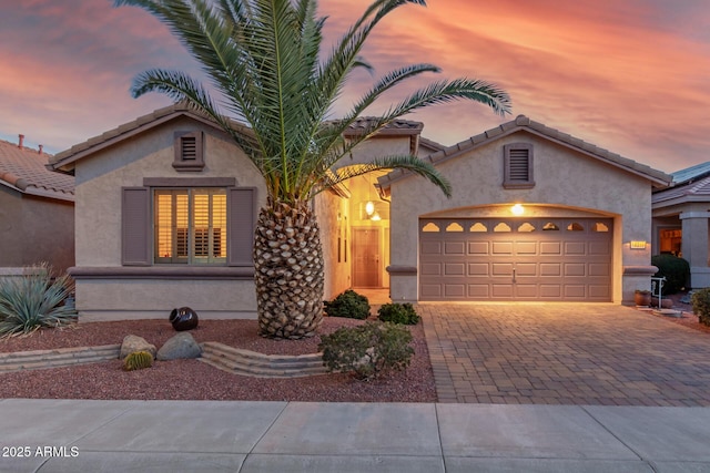 mediterranean / spanish-style home featuring a garage, decorative driveway, a tile roof, and stucco siding