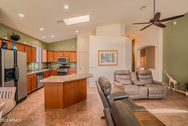 kitchen with light stone counters, a kitchen island, a sink, open floor plan, and appliances with stainless steel finishes