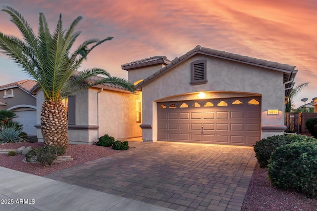 mediterranean / spanish-style home with decorative driveway, a tiled roof, an attached garage, and stucco siding