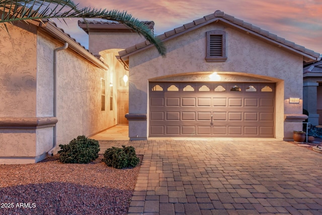 exterior space featuring decorative driveway, a tile roof, an attached garage, and stucco siding