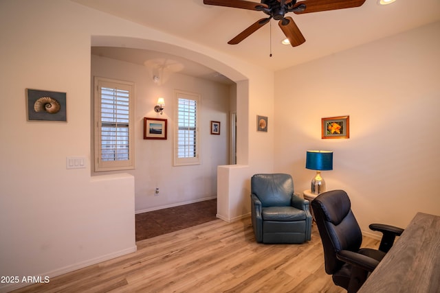 home office featuring arched walkways, ceiling fan, light wood-type flooring, and baseboards