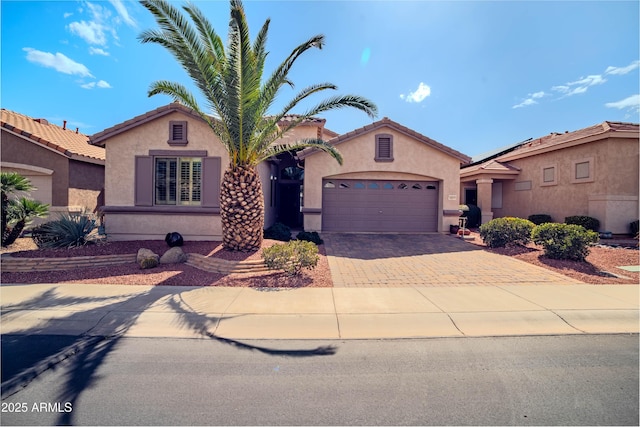 mediterranean / spanish-style house featuring an attached garage, a tile roof, decorative driveway, and stucco siding