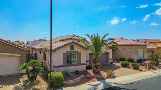 mediterranean / spanish house featuring a garage, a tiled roof, decorative driveway, and stucco siding