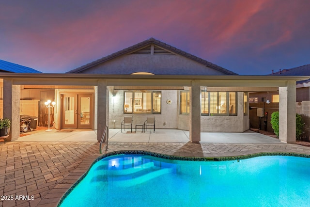 pool at dusk with a patio area and an outdoor pool