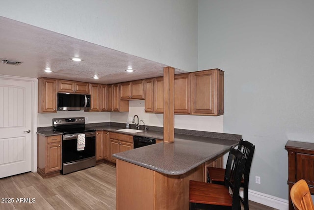 kitchen featuring sink, light hardwood / wood-style flooring, kitchen peninsula, and appliances with stainless steel finishes