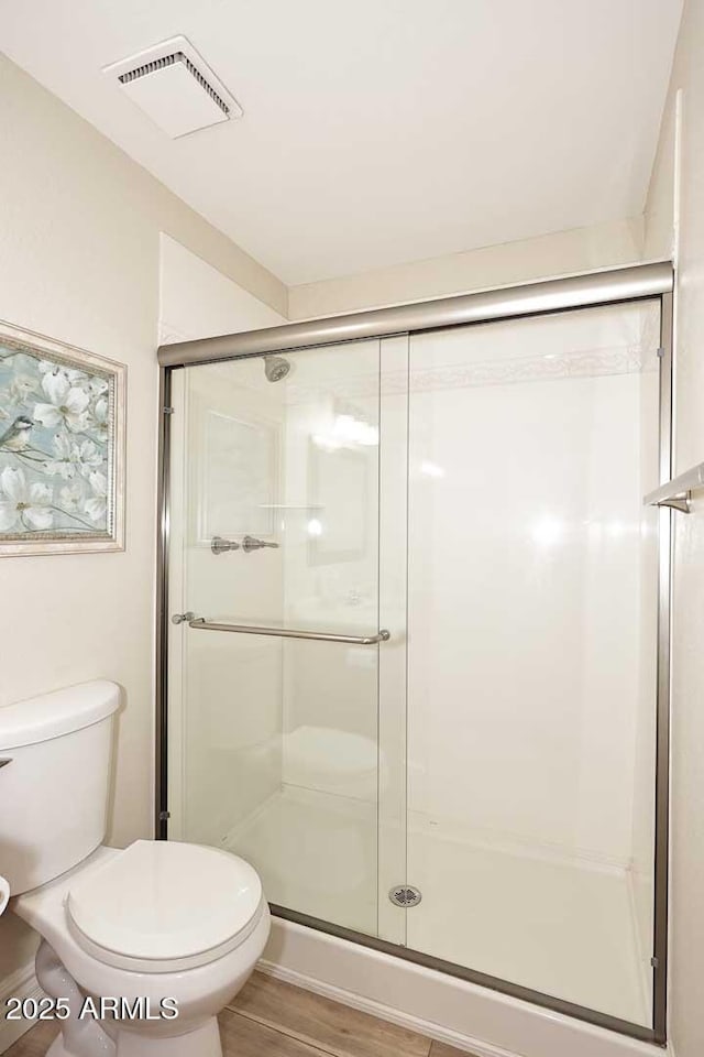 bathroom with hardwood / wood-style floors, a shower with shower door, and toilet