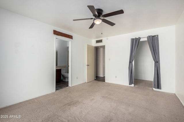 unfurnished bedroom featuring ensuite bath, carpet, visible vents, and ceiling fan