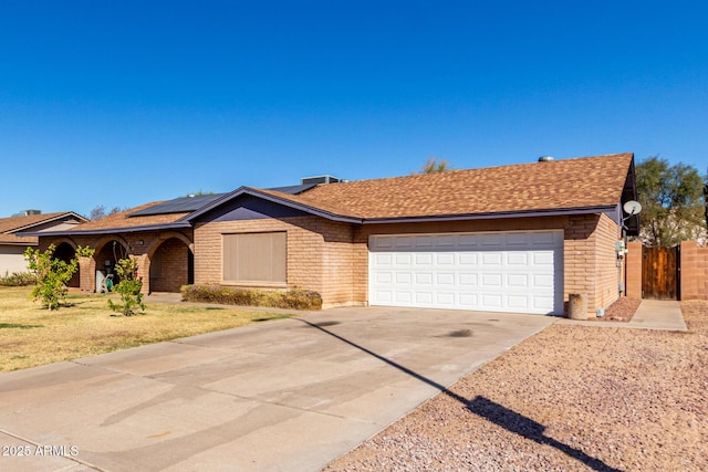 ranch-style home featuring a garage, a shingled roof, fence, concrete driveway, and roof mounted solar panels