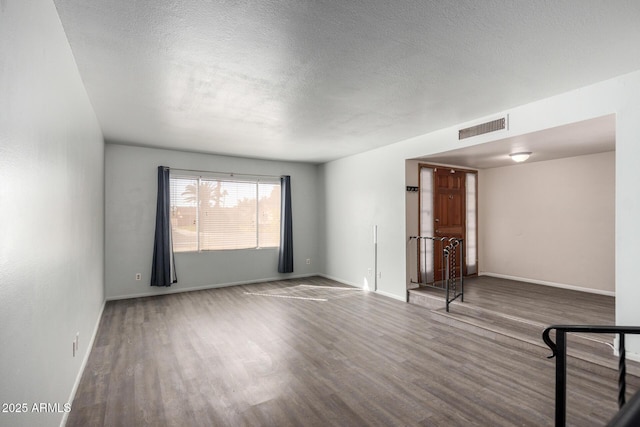 empty room featuring visible vents, a textured ceiling, baseboards, and wood finished floors