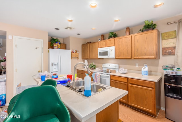 kitchen with a kitchen island with sink, sink, light wood-type flooring, light brown cabinetry, and white appliances