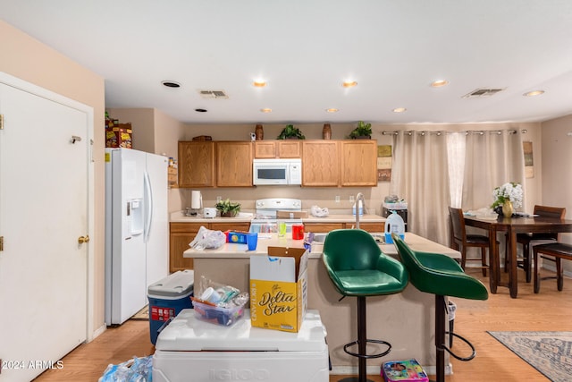 kitchen featuring light hardwood / wood-style floors, a kitchen island with sink, a kitchen breakfast bar, and white appliances