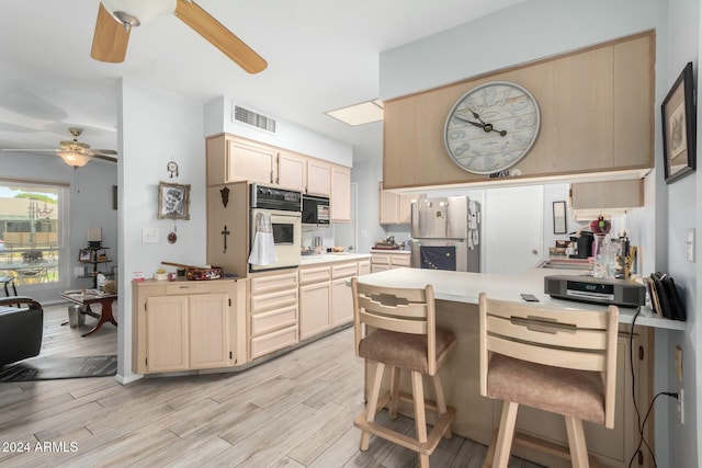 kitchen featuring oven, light hardwood / wood-style floors, a breakfast bar area, and stainless steel refrigerator