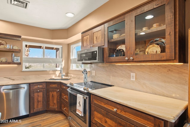 kitchen with backsplash, sink, light hardwood / wood-style flooring, appliances with stainless steel finishes, and light stone counters