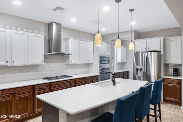 kitchen featuring an island with sink, light wood-type flooring, wall chimney exhaust hood, and hanging light fixtures