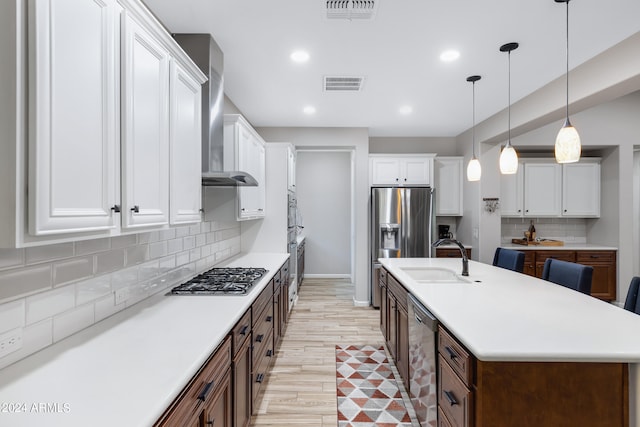 kitchen with an island with sink, sink, white cabinetry, appliances with stainless steel finishes, and light hardwood / wood-style floors