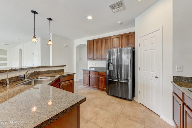 kitchen featuring arched walkways, a sink, visible vents, hanging light fixtures, and stainless steel fridge