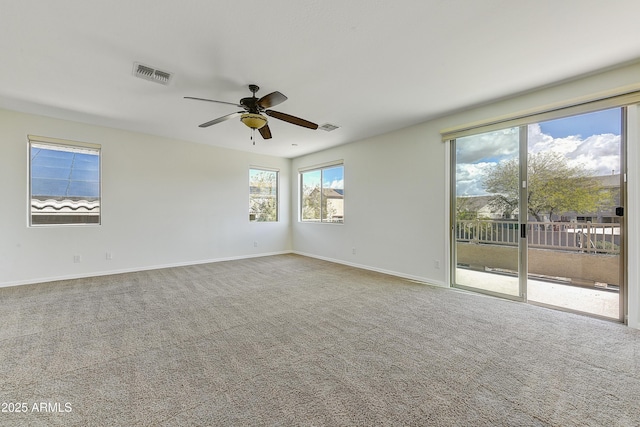 empty room with carpet floors, a ceiling fan, visible vents, and baseboards