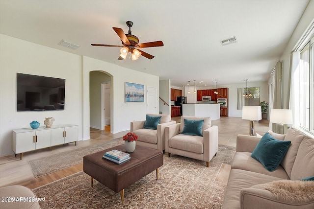 living room with light wood-style floors, arched walkways, visible vents, and ceiling fan